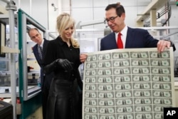 FILE - Treasury Secretary Steven Mnuchin, right, shows his wife, Louise Linton, a sheet of new $1 bills, the first currency notes bearing his and U.S. Treasurer Jovita Carranza's signatures, Nov. 15, 2017, at the Bureau of Engraving and Printing.