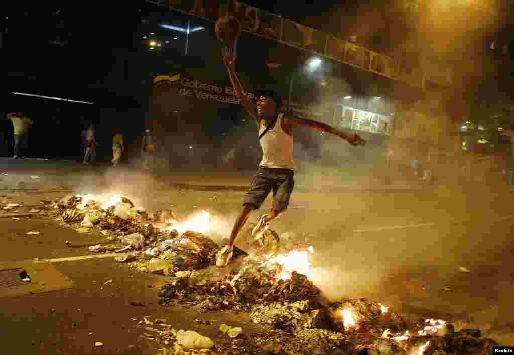 A man jumps over a barricade of burning garbage that supporters of opposition leader Henrique Capriles used to block a street, as they demonstrated for a recount of the votes in Sunday's election, in Caracas, April 15, 2013. 