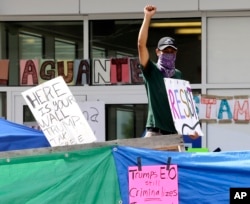 An unidentified man holds a sign behind a makeshift wall at a protest camp on property outside the U.S. Immigration and Customs Enforcement office in Portland, Oregon, June 25, 2018. The round-the-clock demonstration outside the office began June 17.