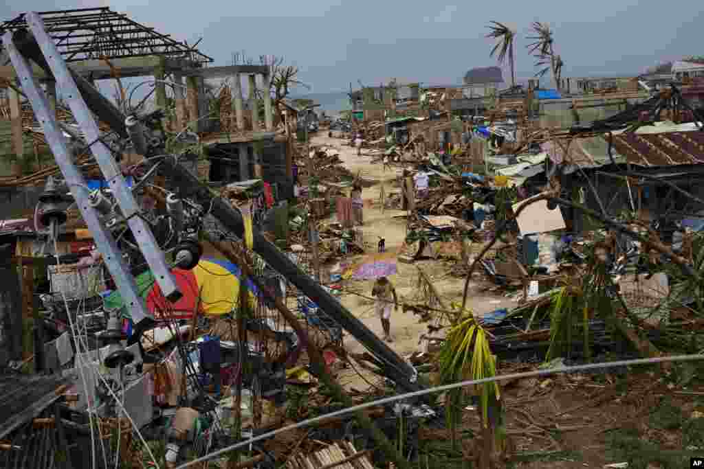 Para penyintas Topan Haiyan berjalan di antara reruntuhan rumah mereka di Maraboth, Filipina (14/11). (AP/David Guttenfelder)