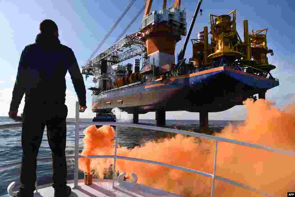 French sailor Clement Brochot stands on the front deck of a fishing boat in front of a drilling platform ship in the Bay of Saint-Brieuc, western France, to protest the planned construction of 62 wind turbines offshore in the bay.
