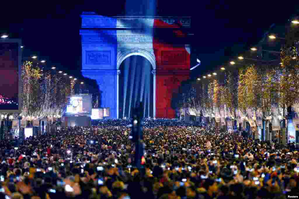 Revelers gather near the Arc de Triomphe, lit in the colors of the French flag, on the Champs Elysees in Paris during New Year's celebrations, Dec. 31, 2015.