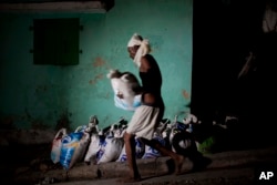 FILE - A "bayakou," or human waste cleaner, carries a sack filled with human waste to be hauled away and dumped before sunrise, in Port-au-Prince, Haiti, Dec. 22, 2016.