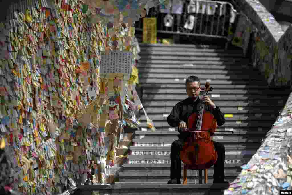 David Wong, pemain cello, tampil di dekat tulisan pada tembok yang memberi dukungan demonstran pro-demokrasi di Hong Kong.