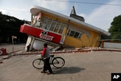 A man walks his bike past a building felled by a 7.1 earthquake, in Jojutla, Morelos state, Mexico, Sept. 20, 2017.