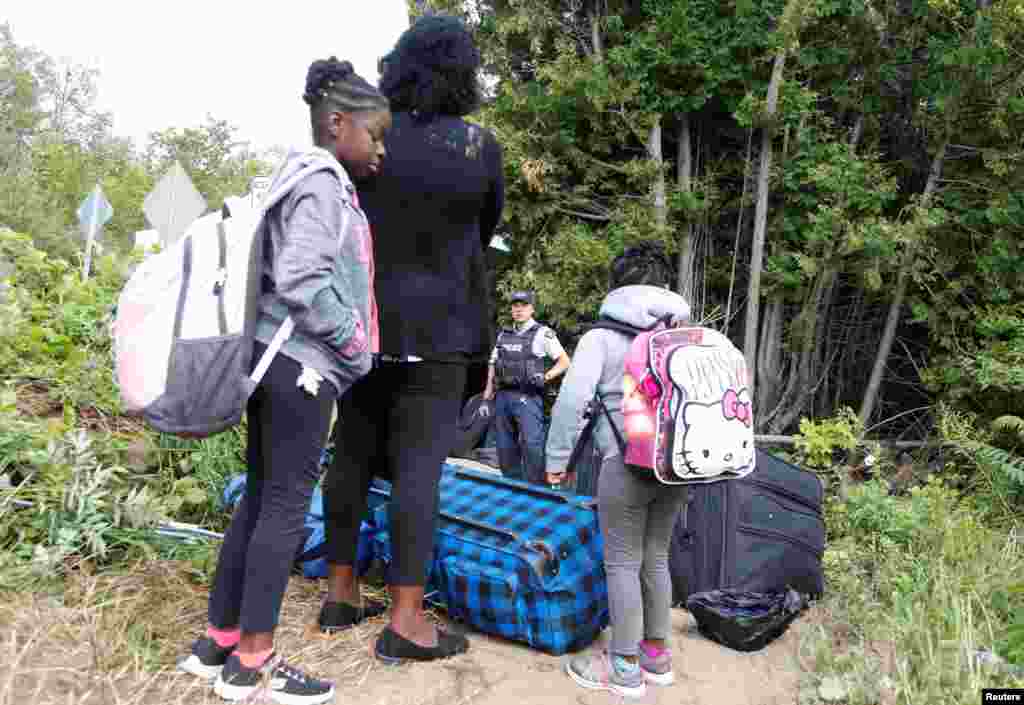 A family who identified themselves as from Haiti are confronted by a Royal Canadian Mounted Police officer as they try to enter into Canada from Roxham Road in Champlain, New York, Aug. 7, 2017. 