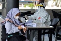 Seorang nakes memeriksa tes sampel usap COVID-19 dari seorang pengunjung di sebuah kedai kopi di Darul Imarah, provinsi Aceh, 24 Mei 2021. (Foto: CHAIDEER MAHYUDDIN / AFP)