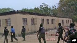 FILE - Security guards walk past a burned-out government secondary school in Chibok, Nigeria, in April 2014.