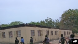 FILE - Security guards walk past a burned-out government secondary school in Chibok, Nigeria. April, 21. 2014.