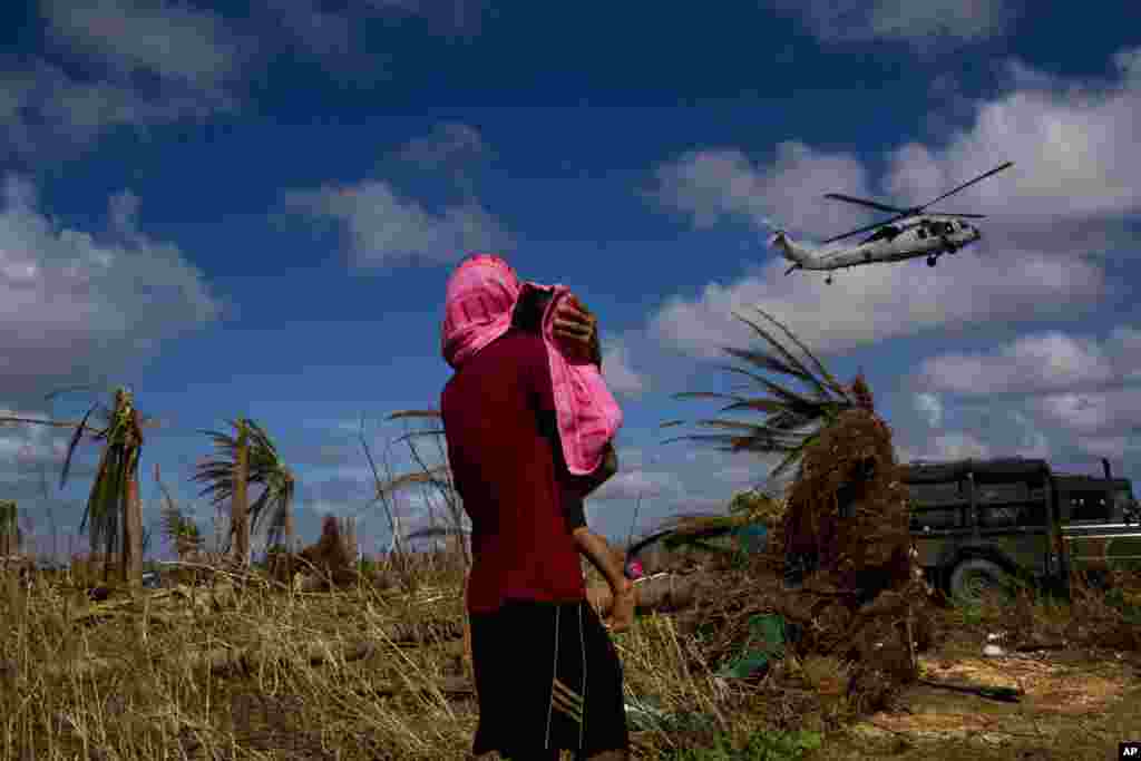 A Typhoon Haiyan survivor carries a child wrapped in a towel as he watches a helicopter landing to bring aid to the destroyed town of Guiuan, Samar Island, Philippines.