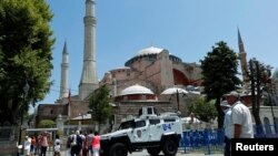 FILE - Tourists enter the Byzantine-era monument of Hagia Sophia as they pass by an armored police vehicle in the Old City of Istanbul, Turkey, July 13, 2016.