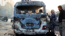 In this photo released by the Syrian official news agency SANA, Syrian security officers gather around a burned bus at the site of a deadly explosion, in Damascus, Syria, Wednesday, Oct. 20, 2021. Two roadside bombs exploded near a bus carrying troops dur