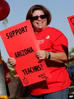 Teacher Ann Russell holds a sign outside Paseo Verde Elementary, April 18, 2018, in Peoria, Ariz. Arizona teachers have voted to walk out of their classrooms to demand more school funding after weeks of growing protests.