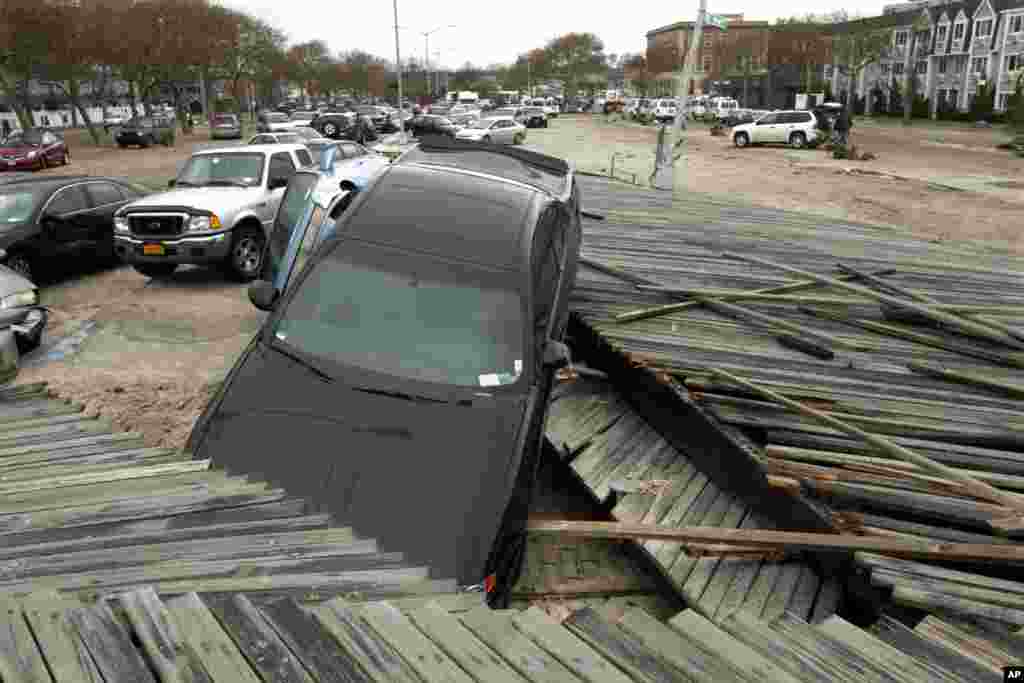 Pedestrians walk past the boardwalk and cars displaced by superstorm Sandy, near Rockaway Beach in the New York City borough of Queens, Oct. 30, 2012, in New York. 