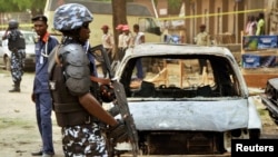 A policeman stands near damaged vehicles after a suicide car bomber killed five people on a street of popular bars and restaurants in Sabon Gari, Kano, Nigeria, May 19, 2014.