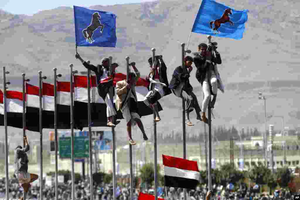 Supporters of Yemen former President Ali Abdullah Saleh climb on flag poles during a rally marking the anniversary of his power handover in Sanaa, Yemen.