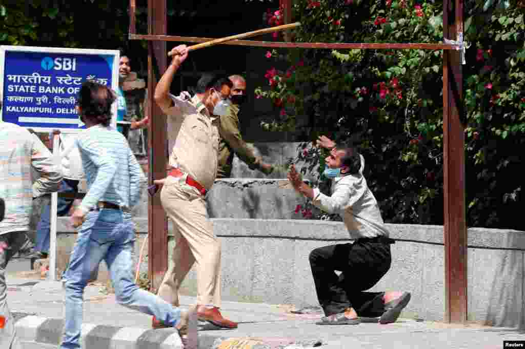 A police officer raises a stick at a man who, police said, broke the social distancing rule, outside a wine shop during an extended nationwide lockdown to slow the spread of the coronavirus disease (COVID-19), in New Delhi, India.