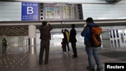 People take pictures of a flight information board displaying the Scheduled Time of Arrival of Malaysia Airlines Flight MH370 (top, in red) at the Beijing Capital International Airport in Beijing, March 8, 2014.