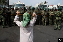 FILE - In this July 7, 2009 photo, a Uigher woman demands the return of members from her community before a group of paramilitary police officers when journalists visited the area in Urumqi in western China's Xinjiang province.