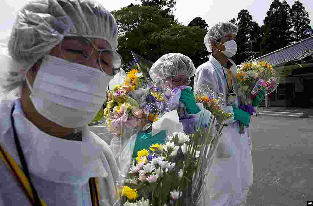 Mourners in protective suits hold flowers at a memorial ceremony for residents from the town of Okuma, inside the contaminated exclusion zone near the crippled Fukushima Daiichi nuclear power plant, July 24, 2011.&nbsp;