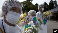 Mourners in protective suits hold flowers at memorial for residents of Okuma, a small town near Fukushima Dai-Ichi nuclear power plant, Japan, July 2011.
