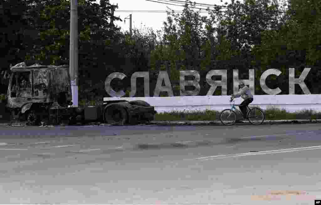 A man rides a bicycle past a sign reading "Slovyansk" and charred remains of a truck on a road leading into Slovyansk, May 6, 2014.