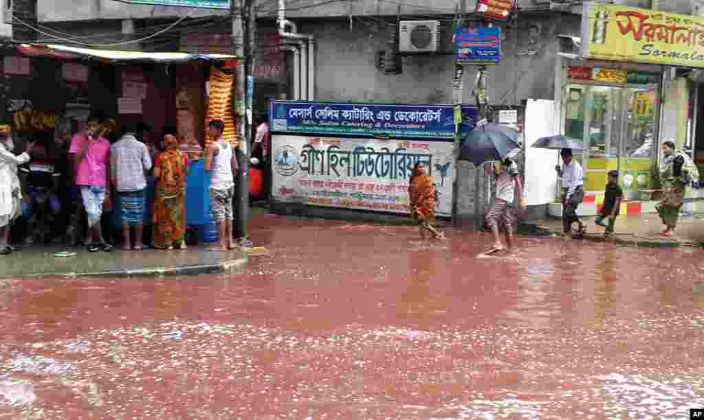 People wade through a road turned red with blood from sacrificial animals on Eid al-Adha that mixed with water from heavy rainfall, in Dhaka, Bangladesh.