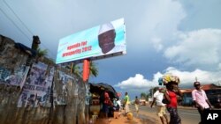 People walk past a campaign poster for incumbent President Ernest Bai Koroma, in Freetown, Sierra Leone, Oct. 19, 2012. 
