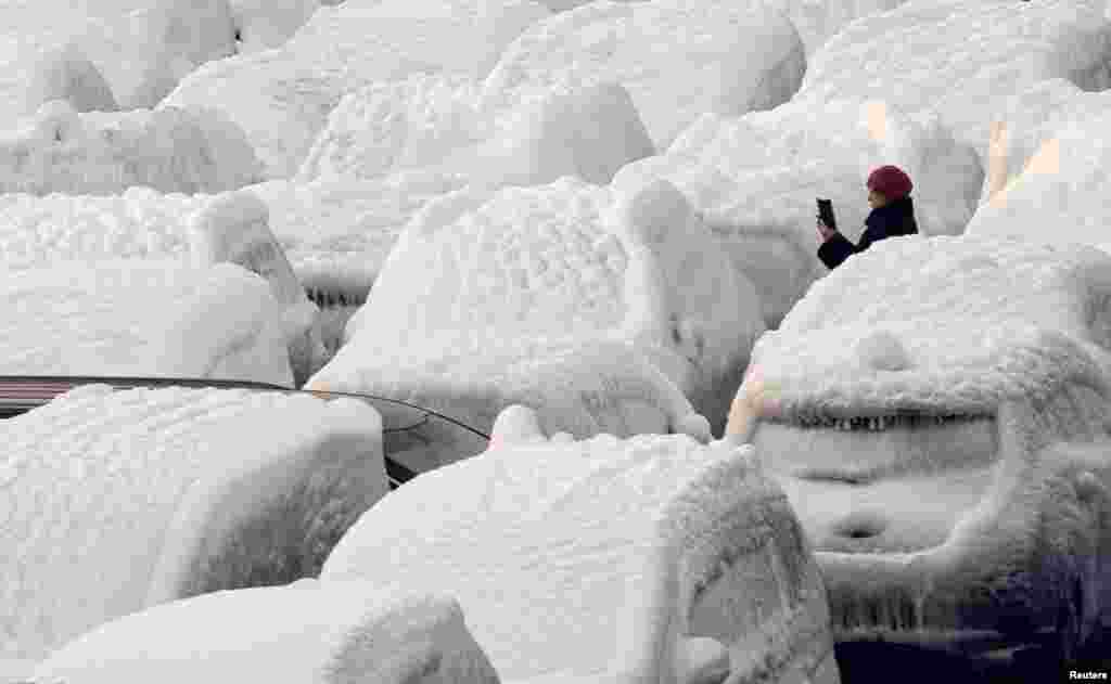 A woman takes a picture of ice-covered vehicles unloaded from the cargo ship Sun Rio, which was caught in severe weather conditions in the Sea of Japan, in the port of Vladivostok, Russia, Dec. 29, 2021.