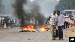 Two men carry a suitcase past a burning barricade in Bujumbura, Burundi, April 30, 2015, after the government issued and ordered for all university campuses to close down.