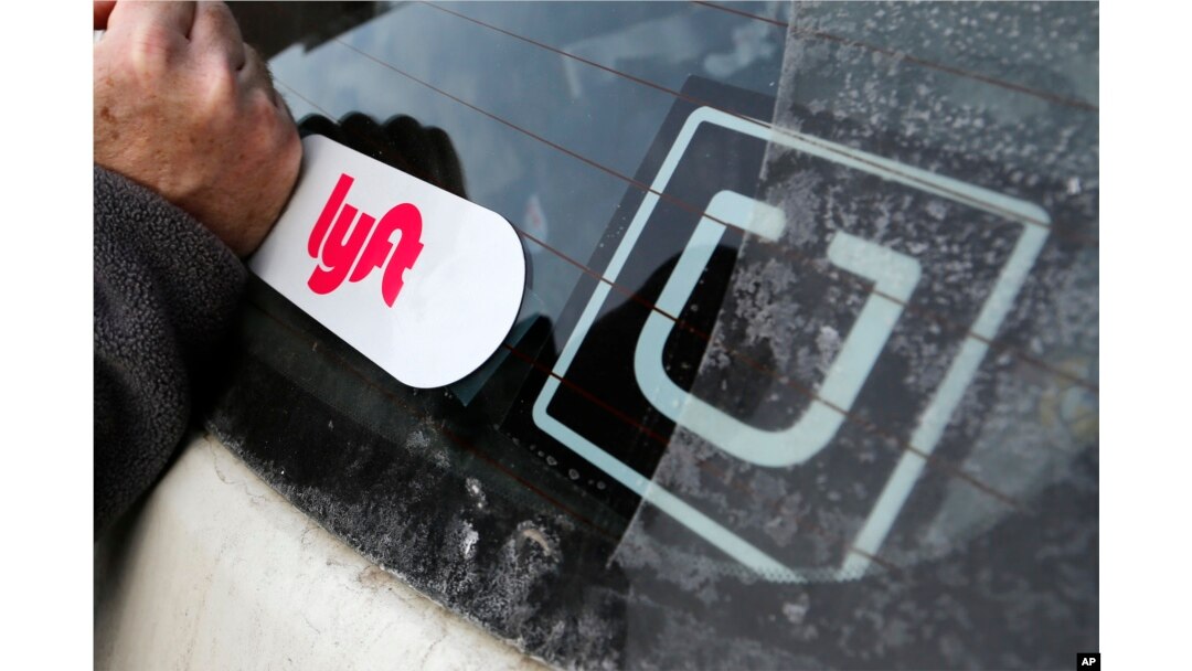 FILE - A Lyft logo is installed on a Lyft driver's car next to an Uber sticker in Pittsburgh, Jan. 31, 2018.