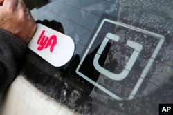 FILE - A Lyft logo is installed on a Lyft driver's car next to an Uber sticker in Pittsburgh, Jan. 31, 2018.