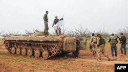 Rebel fighters walk past an armored vehicle carrying the flag of the Tahrir al-Sham rebel alliance near the town of Maardes in the countryside of the central Syrian province of Hama, March 22, 2017. Tahrir al-Sham, an al-Qaida offshoot, has recently emerged as the most powerful Sunni insurgent faction in Syria after consolidating its control over most of the northwestern province of Idlib.