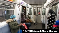 Des personnes portant des masques pour contrer l'épidémie de COVID-19, sont dans une cabine de train à la station de métro Times Square à New York, États-Unis, le 17 avril 2020. REUTERS / Jeenah Moon