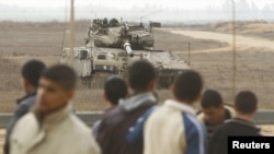 Palestinians stand close to the fence as an Israeli tank is seen on the border between Israel and southern Gaza Strip, November 23, 2012.