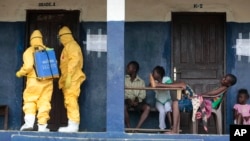 Residents of a West African village watch as members of a response team disinfect an area as they pick up suspected Ebola patients that had been quarantined, Sept. 30, 2014.