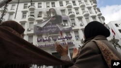 Women applause as they look at a torn banner depicting former Tunisian President Zine El Abidine Ben Ali in the center of Tunis, Sunday, Jan. 16. 2011.