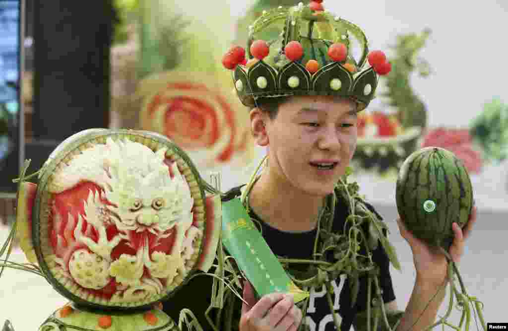 A man wearing a headpiece made of watermelon peel stands next to a watermelon sculpture during an annual watermelon festival in Daxing district, Beijing, China, May 25, 2015.