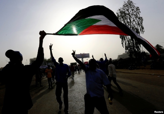 Sudanese demonstrators wave their national flag as they arrive for a protest rally demanding Sudanese President Omar Al-Bashir to step down outside the Defense Ministry in Khartoum, Sudan, April 11, 2019.