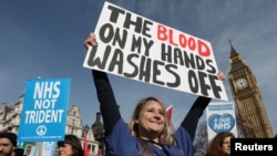 FILE - A junior doctor poses with a banner as she takes part in a demonstration to demand more funding for Britain's National Health Service (NHS), in London, March 4, 2017.