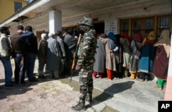 An Indian paramilitary soldier stands guard as Kashmiri voters wait in a queue to cast their votes outside a poling station on the outskirts of Srinagar, Indian-controlled Kashmir, April 18, 2019.