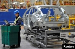 FILE - An employee uses a laptop next to a car body at an assembly line at a Ford manufacturing plant in Chongqing municipality, China.