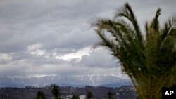 The Caucasus Mountains, site of several 2014 Winter Olympic events, rise in the background as a palm tree stands in the Coastal Cluster's Olympic Park in Sochi, Russia, Jan. 30, 2014.