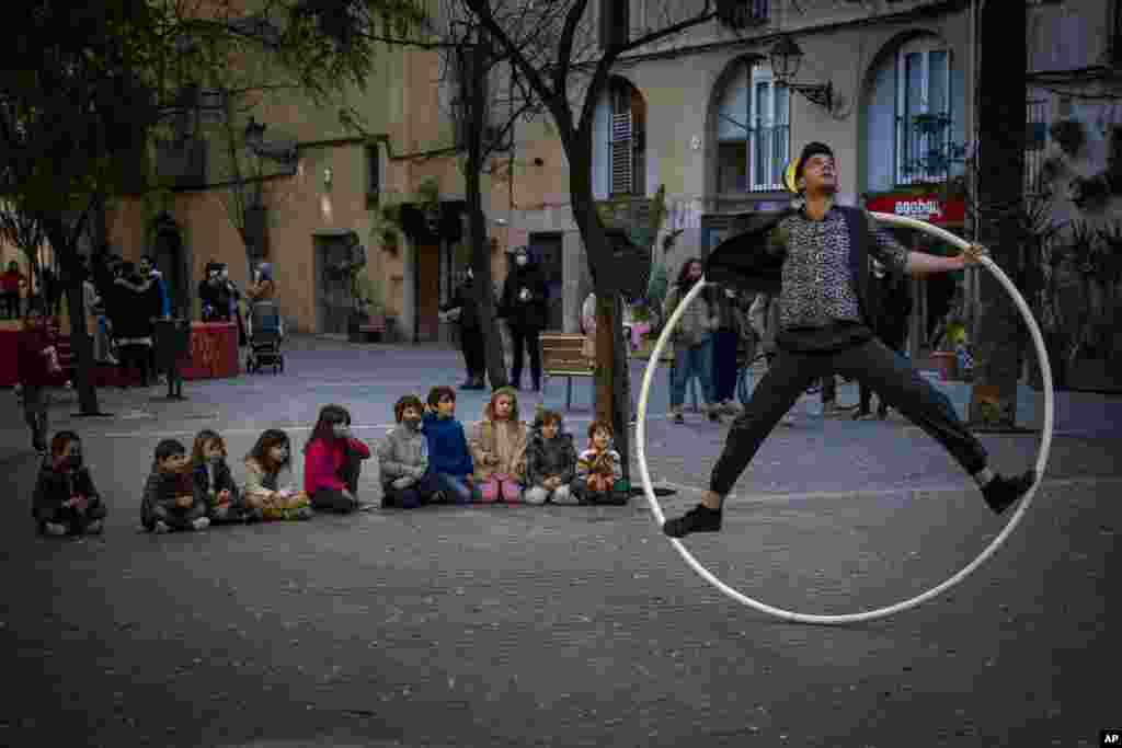 Children sit on the ground as they watch a street circus artist performing with a ring in Barcelona, Spain.