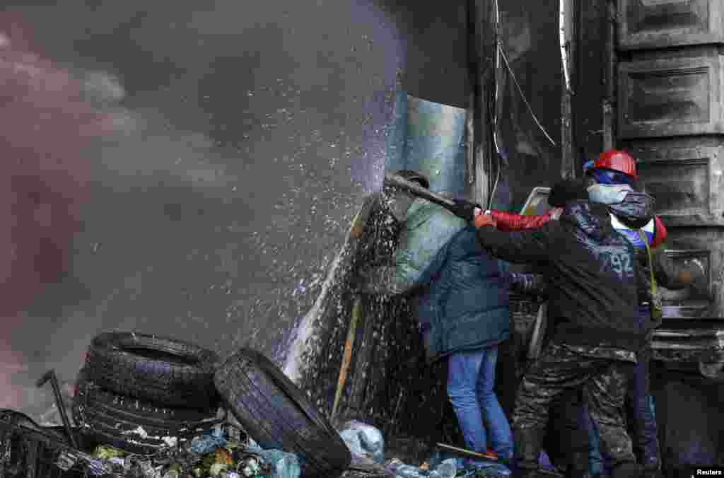 Pro-European integration protesters take cover from water sprayed from a fire engine during clashes with riot police in Kyiv, Jan. 23, 2014.