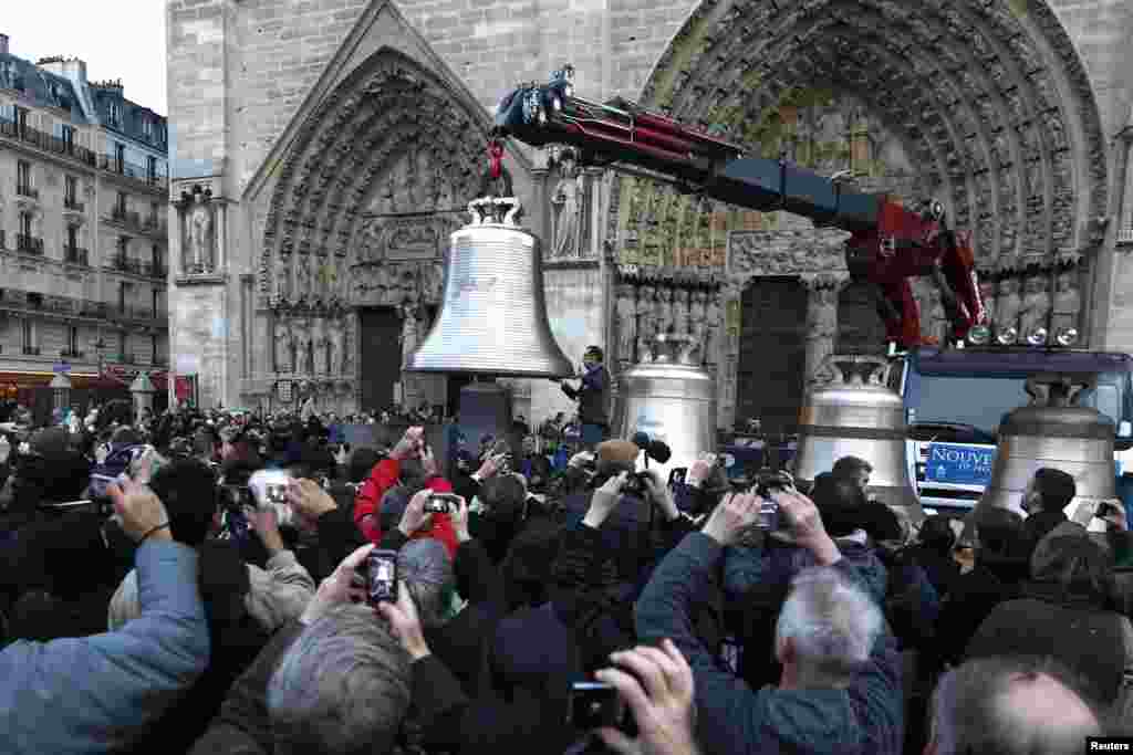 The public takes photographs of &#39;Gabriel&#39;, the new and biggest bell, as it is hoisted from a trailer truck in front of Notre-Dame de Paris Cathedral in Paris, France, after being transported with the seven other replacement bronze bells from Normandy.