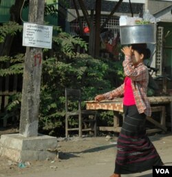 Một người phụ nữ mặc longyi bôi thanaka trên má bưng một thúng đồ ăn trên đầu. (Steve Herman/VOA News)