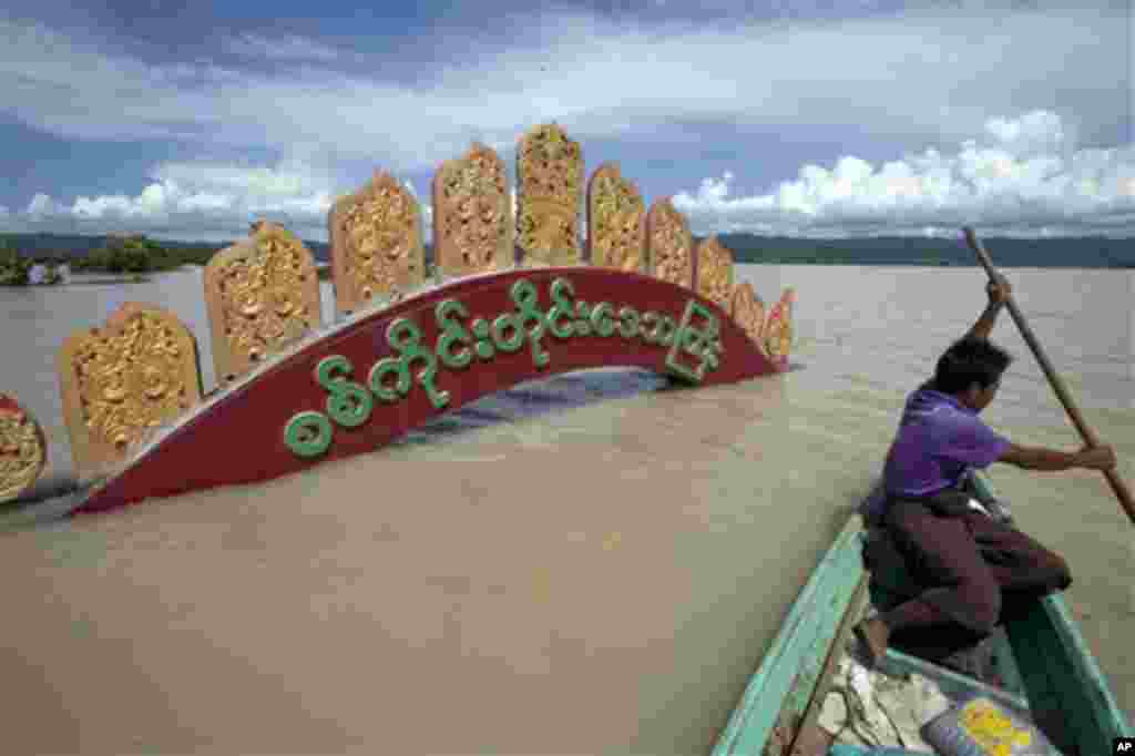 A man rows his boat by the entrance signboard of Kalay township submerged in water, in Sagaing, Myanmar, Sunday, Aug. 2, 2015. Heavy rains in Myanmar have caused more flooding, devastating several townships and forcing more than 18,000 people into tempora