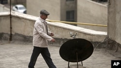 An Iranian man walks past a satellite dish on a rooftop in northern Tehran, January 15, 2011.