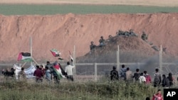 Protesters wave Palestinians flags in front of Israeli solders on Gaza's border with Israel, east of Beit Lahiya, Gaza Strip, April 4, 2018.